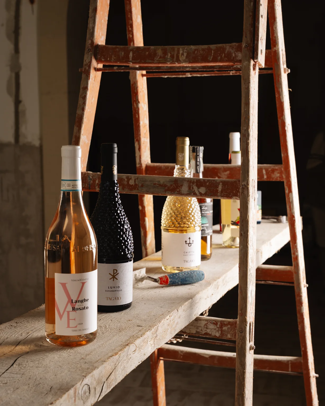 Bottiglie di vino su una scaletta rustica, tra cui un Langhe Rosato e un Luvio Susumaniello Tagaro