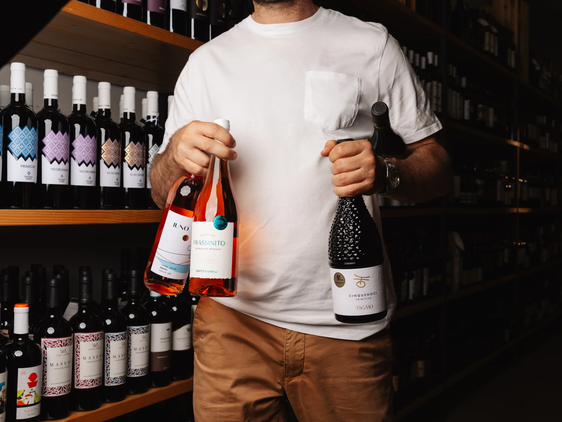 Bottiglie di vino tra le mani con in sfondo un'enoteca elegante e accogliente